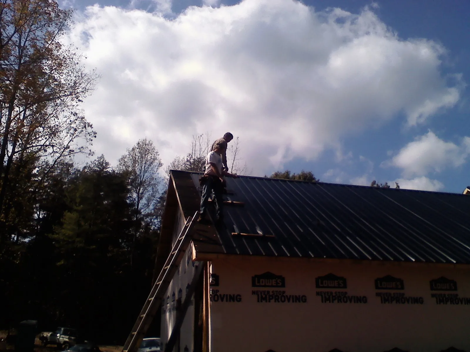 Roofer fastening dark metal panels high against a cloudy sky, from a Roof Inspection job in Government Camp