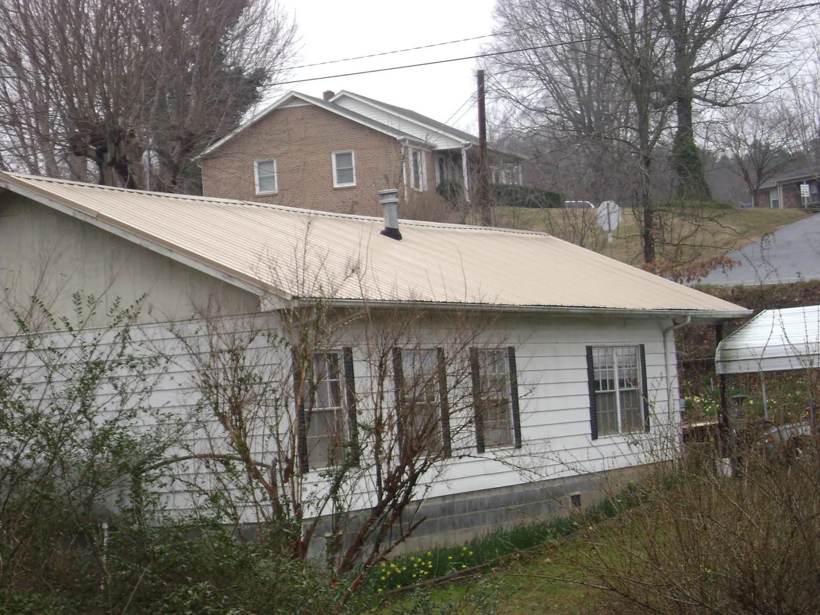 Tan metal roof on a white sided house set into a hillside — Commercial Roofing by Roofing Brothers in Government Camp